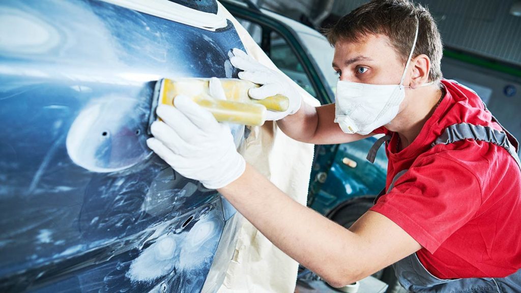 Young man with bright red shirt sanding a car panel in collision centre